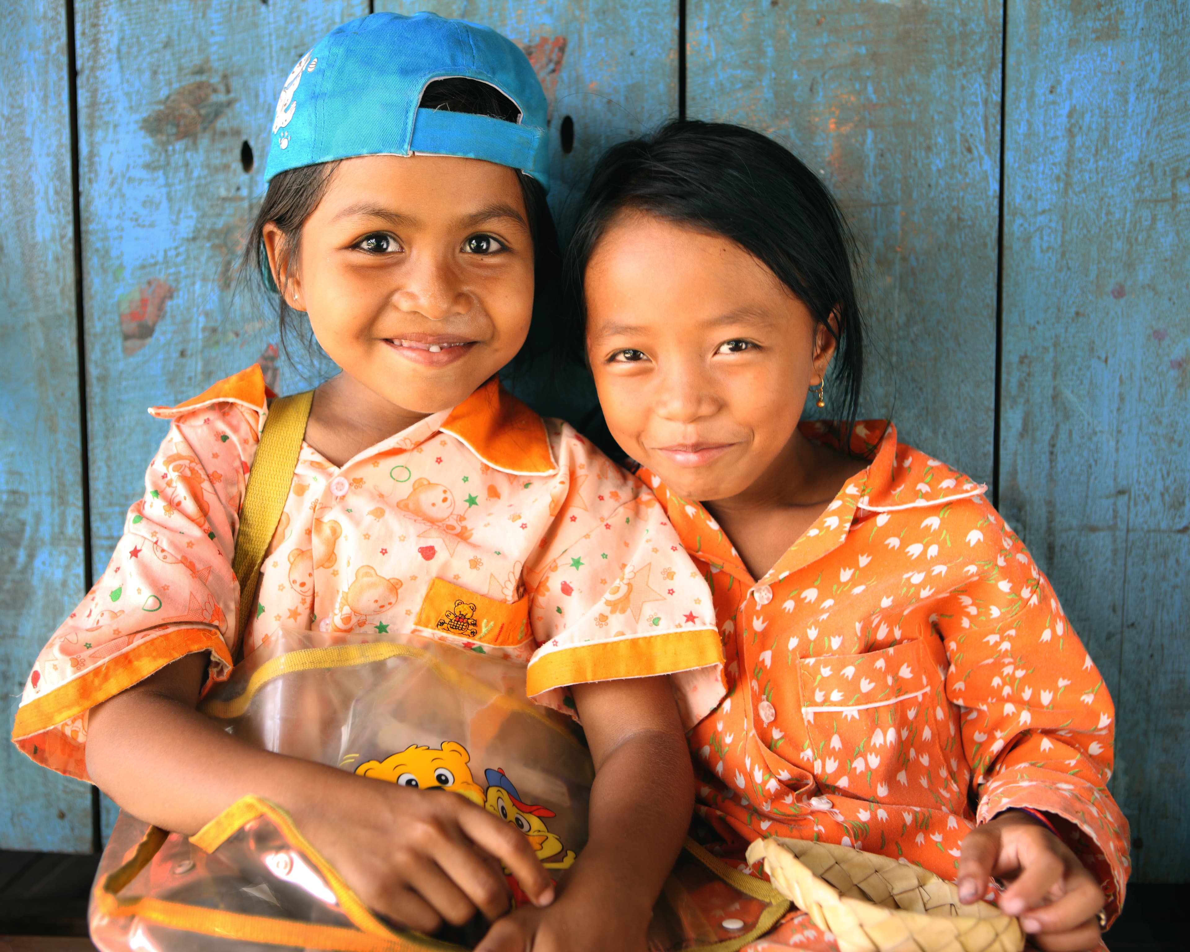Two young girls smiling against a blue wall in Cambodia