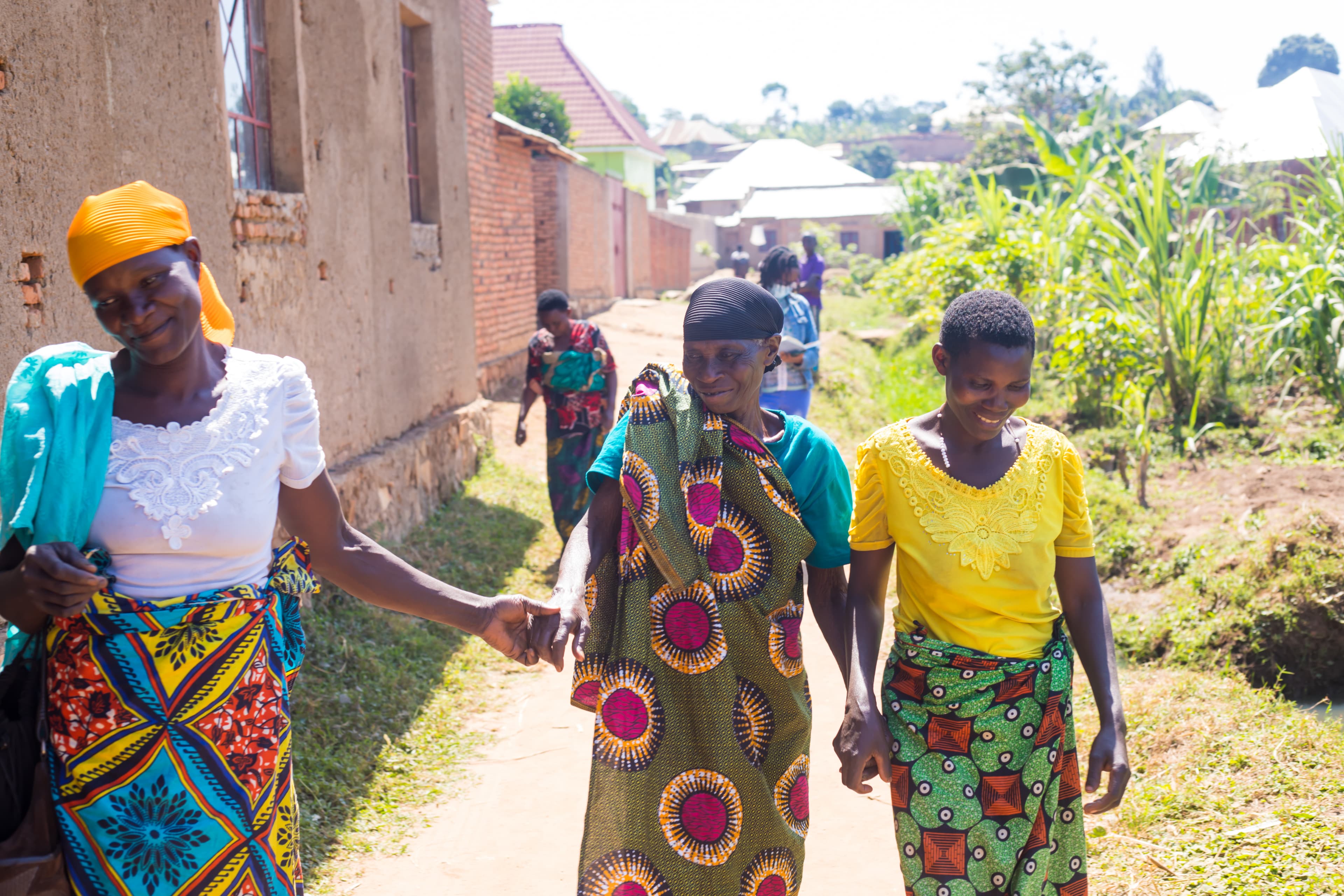 Three women in colorful traditional clothing walking together through a village