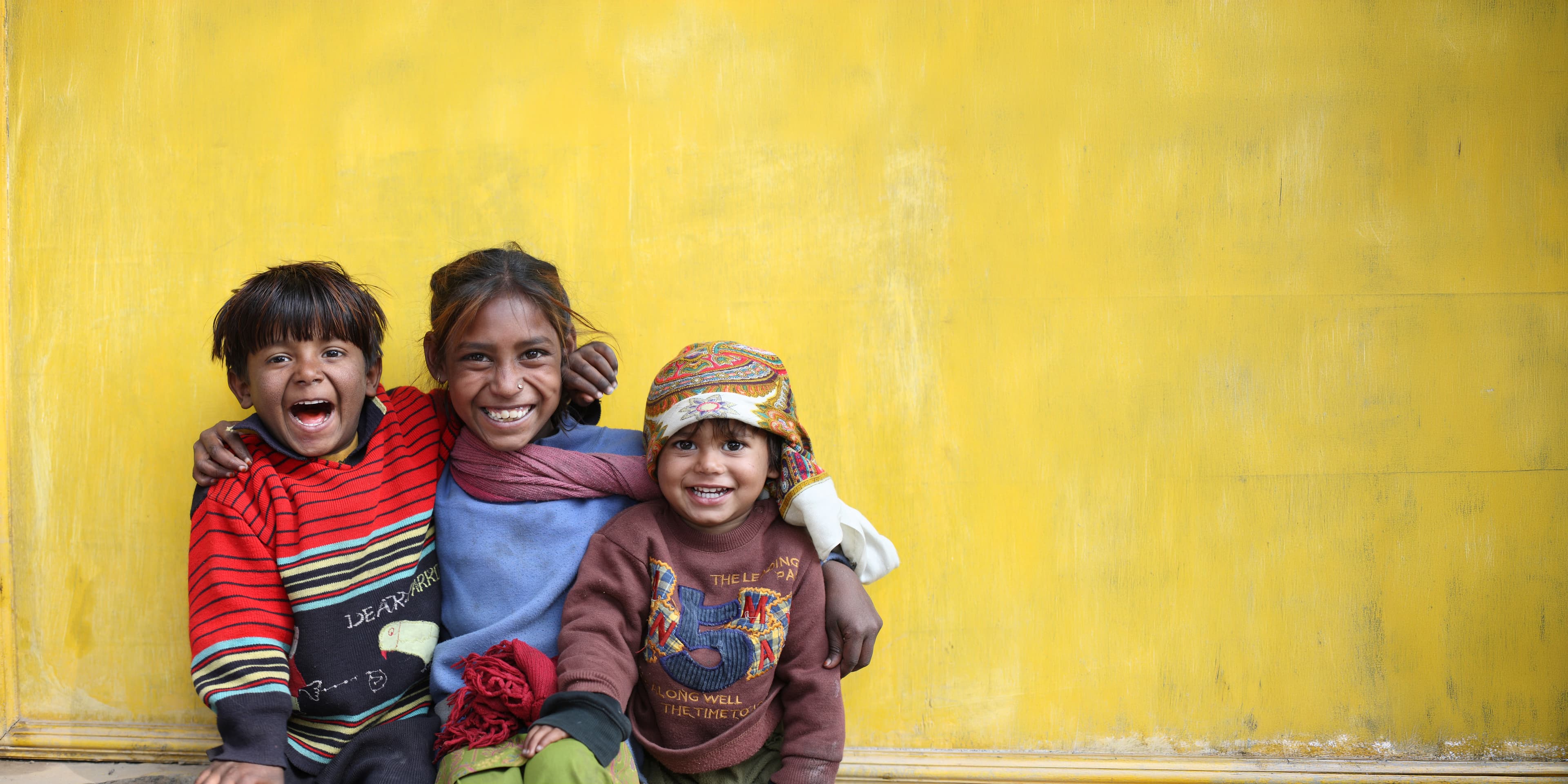 Three children laughing against a yellow wall in Nepal