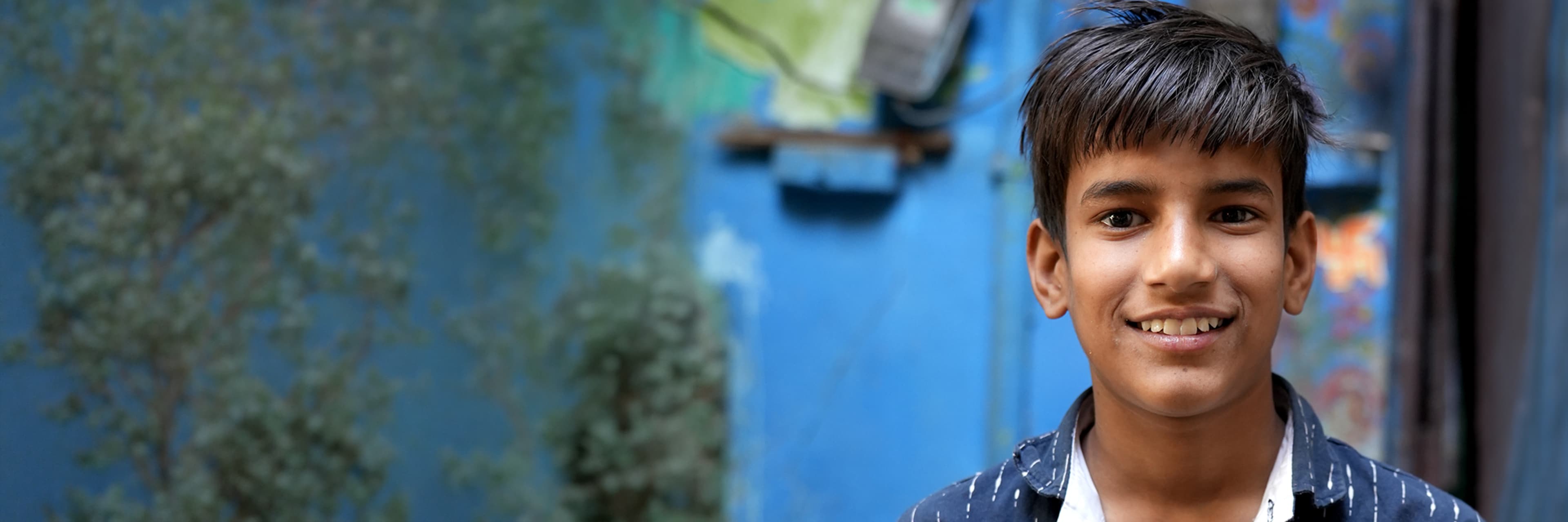 A teenage boy smiling against a blue weathered wall